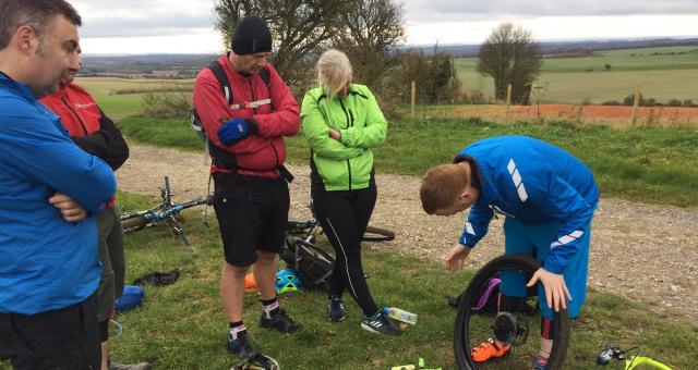 Four people are watching a man removing a tyre from a bike wheel