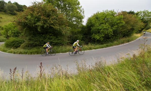 Two riders in close pursuit come out of a steep corner into a climb on a country road in the Surrey Hills